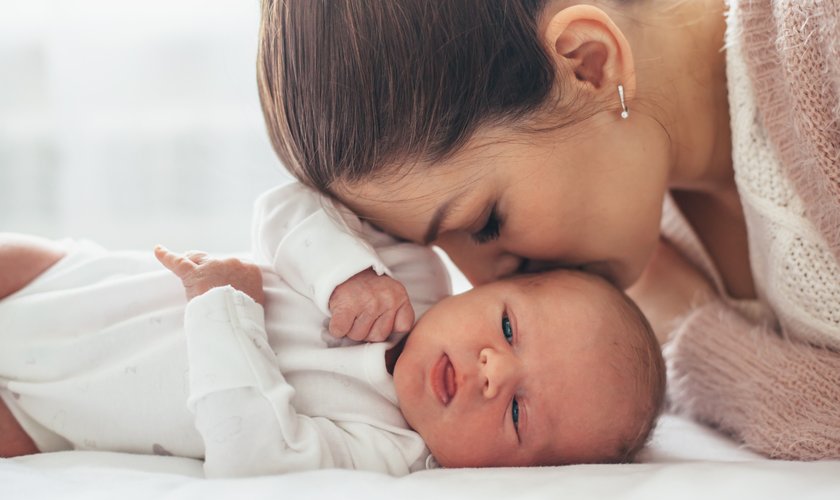 Une maman penchée sur son nouveau-né, le front contre le sien, dans la lumière douce d’une chambre